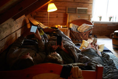 High angle view of male and female friends using smart phones while lying in cottage