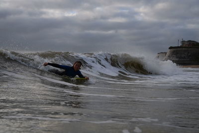 Woman surfboarding on waves in sea against sky