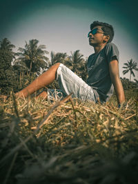 Boy looking away while sitting on land against sky