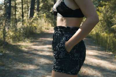 Midsection of sensuous woman with hand in pocket standing in forest