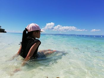 Girl sitting in sea against sky