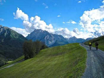 Rear view of people riding cycle with mountains in background