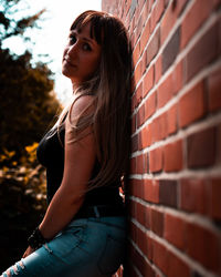 Portrait of woman standing by brick wall