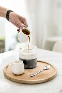 Close-up of hand pouring coffee cup on table