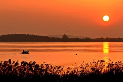 Person on boat in lake against orange sky