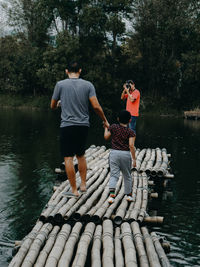 Rear view of men standing by lake against trees