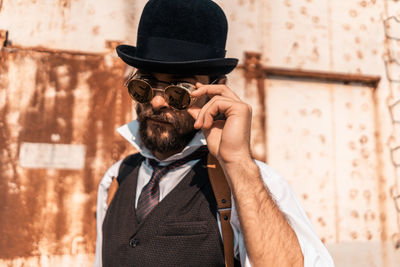 Portrait of man holding hat standing against wall