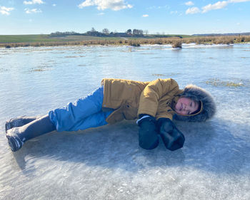 Full length of boy lying down on frozen lake during winter