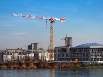 Cranes on river against buildings in city