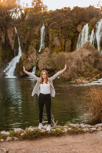 Full length portrait of young woman standing on rock against lake