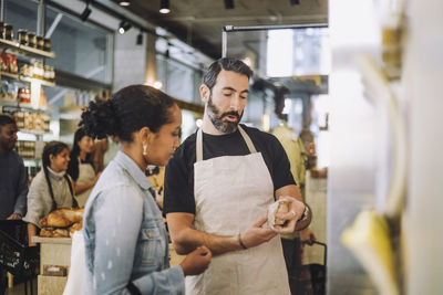 Mature salesman discussing over product with female customer at delicatessen