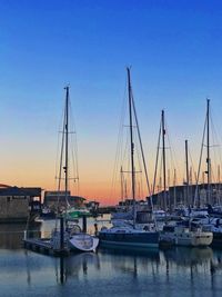 Sailboats moored in harbor at sunset