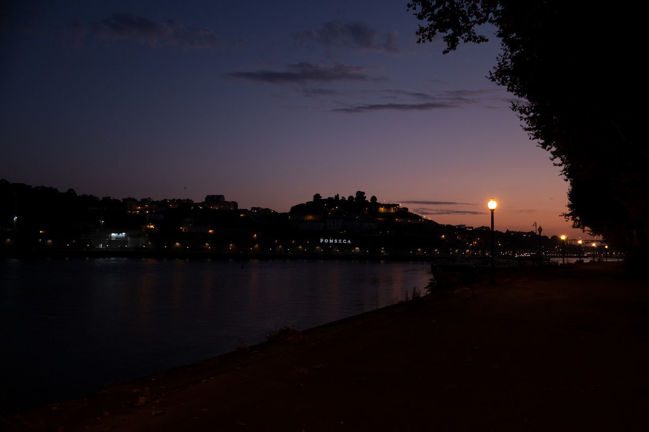 ILLUMINATED CITY BY RIVER AGAINST SKY AT SUNSET