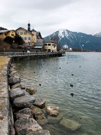 Scenic view of lake by buildings against sky during winter