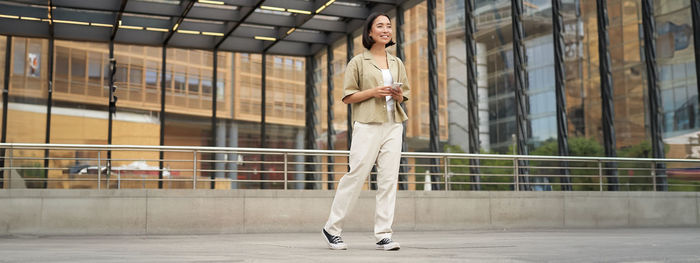 Full length of young woman standing against building