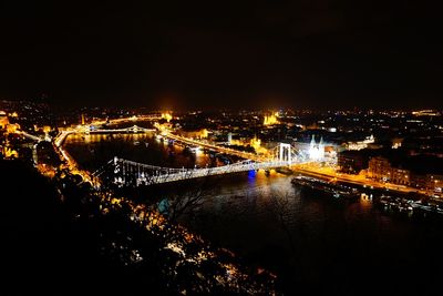 Illuminated city by sea against sky at night