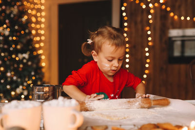 A little girl in red pajamas cooks and eats christmas cookies in the decorated kitchen of the house