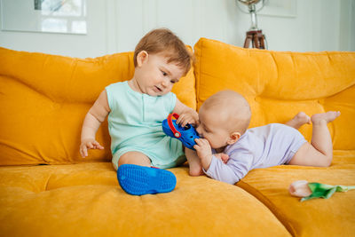 Two babies playing on a yellow sofa