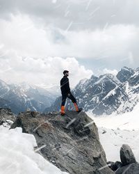 Rear view of man walking on snowcapped mountains against sky