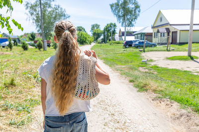 A girl with long hair walks to a store along a village road. eco mesh bag, macrame. eco concept. 