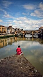 Rear view of woman sitting on bridge over river against sky