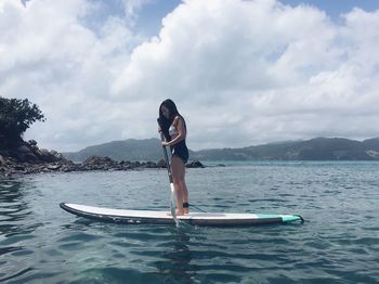 Woman on surfboard in sea against sky