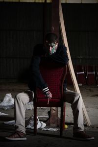 Portrait of hipster sitting on chair while showing obscene gesture in abandoned building