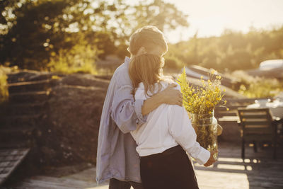 Rear view of friends standing with flower bouquet at harbor