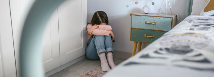 Unrecognizable girl crying on the floor in her bedroom