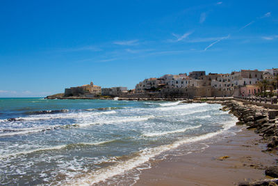 Buildings by sea against blue sky