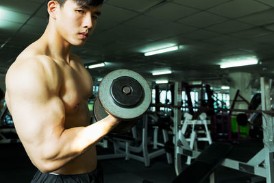 Shirtless muscular man lifting dumbbell while exercising at gym