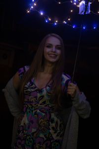 Smiling young woman standing against illuminated lights at night