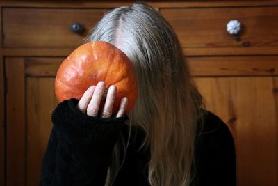 Close-up of woman holding pumpkin against wall