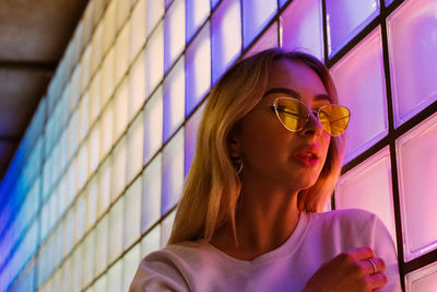 Portrait of young woman wearing sunglasses against wall