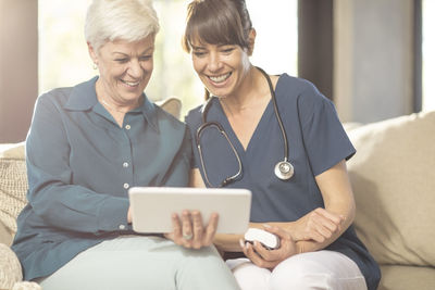 Senior woman sharing tablet with nurse at home