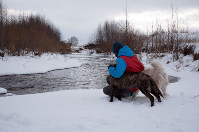 Side view of young woman with dog crouching on snowy field against cloudy sky