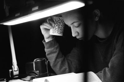 Woman holding coffee cup while reading book on table