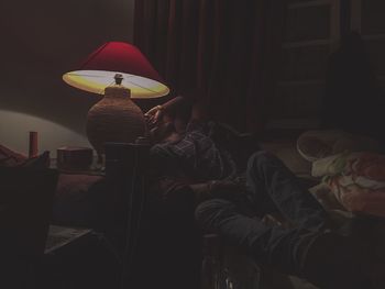 Tired man lying on bed by illuminated electric lamp at home