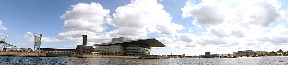 Panoramic view of bridge over river by buildings against sky