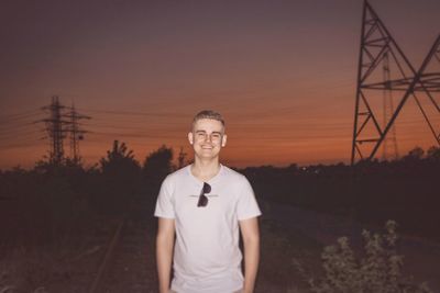 Portrait of young man standing on field against sky during sunset