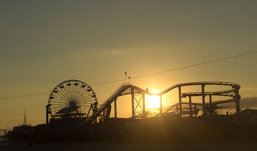 Silhouette of amusement park rides against sky during sunset