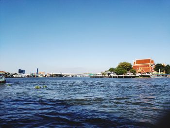 Buildings by sea against clear blue sky