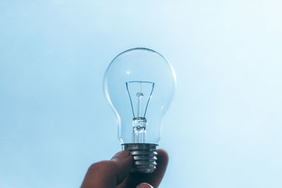 Cropped hand of person holding light bulb against blue background