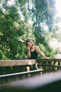 Smiling woman standing by railing against trees