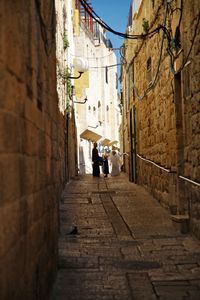 Rear view of people walking on narrow street amidst buildings