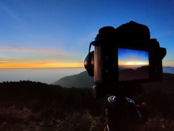 Close-up of camera on landscape against sky during sunset