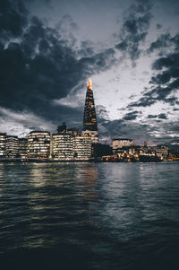 View of city at waterfront against cloudy sky