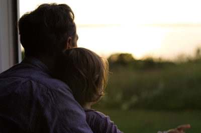 Rear view of father and daughter looking at sunset through window