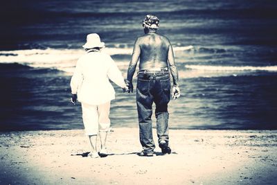 Rear view of two people walking on beach