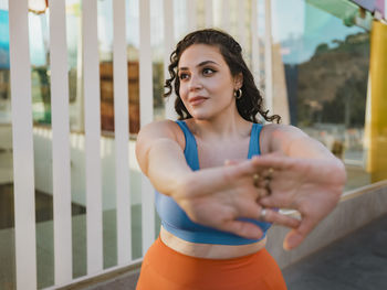 Young woman in sports clothing stretching arms near building